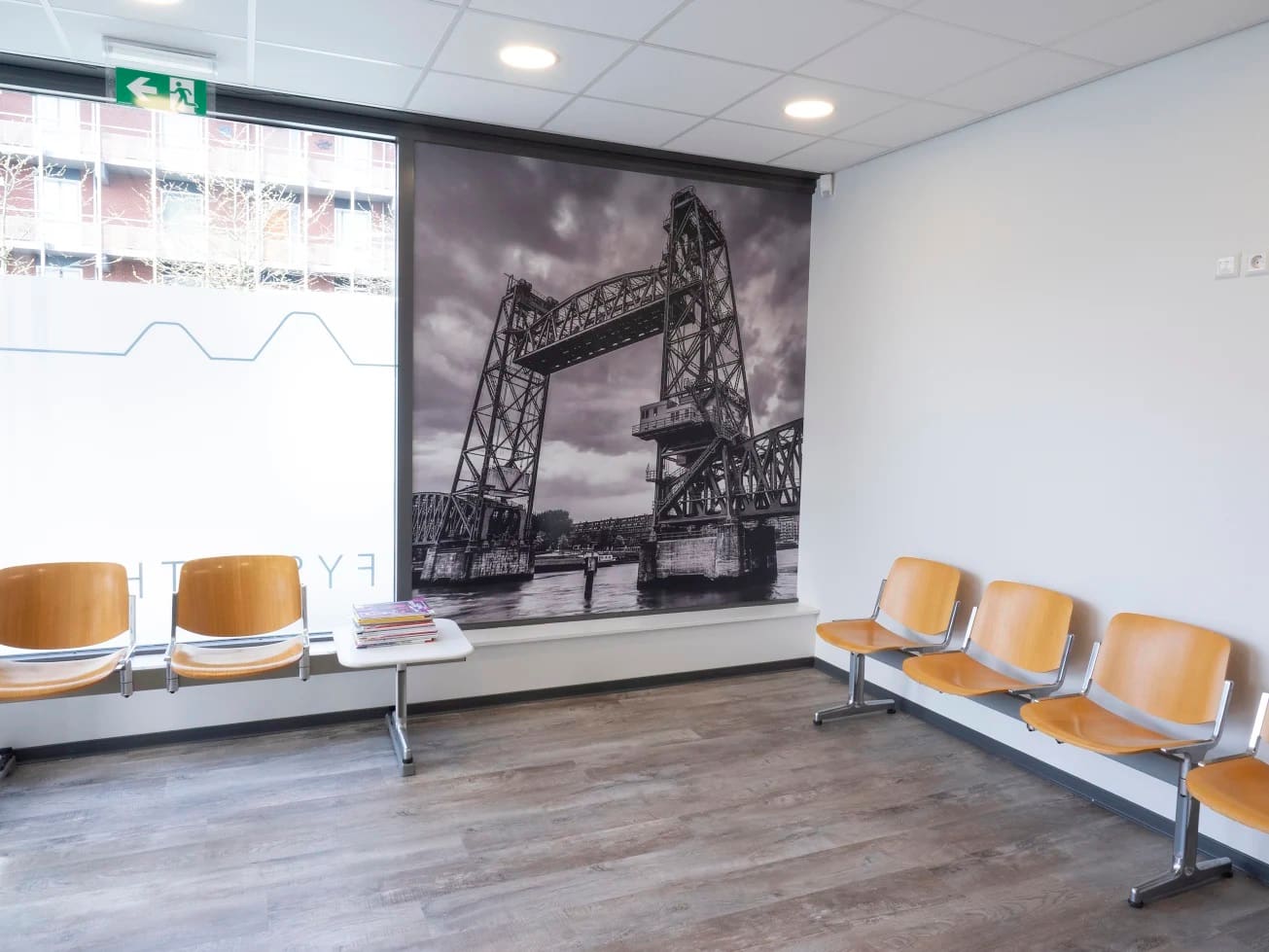 De wachtkamer met houten stoelen en een grote fotowand van de Koningshavenbrug in Rotterdam.