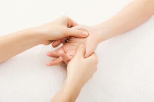 Twee handen van een therapeut masseren de handpalm van een patiënt.